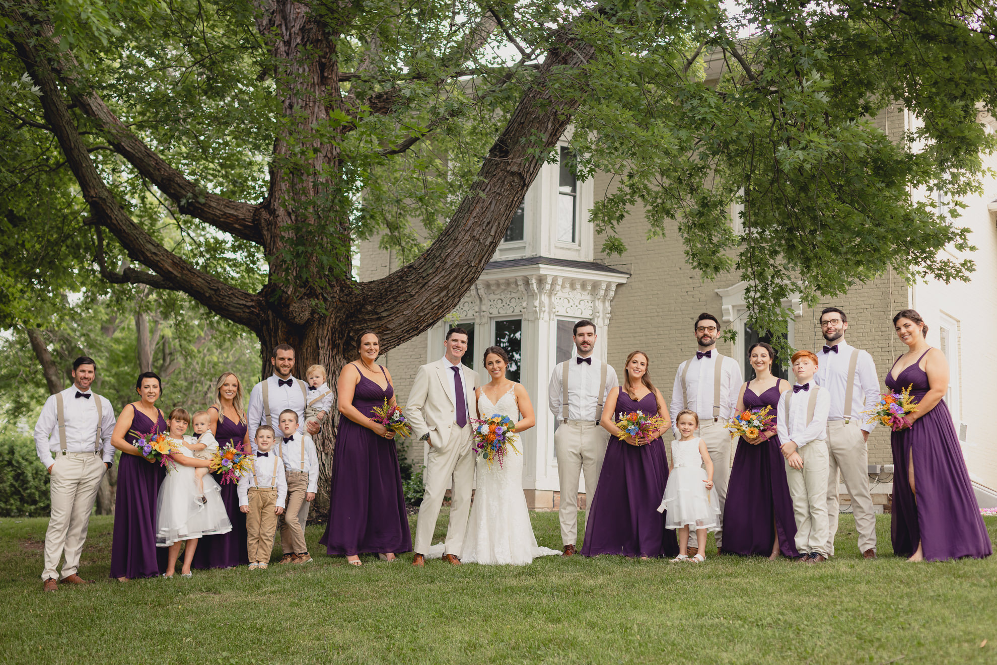 wedding party poses for portrait outside historic house at The Gallagher Barn in Medina, NY