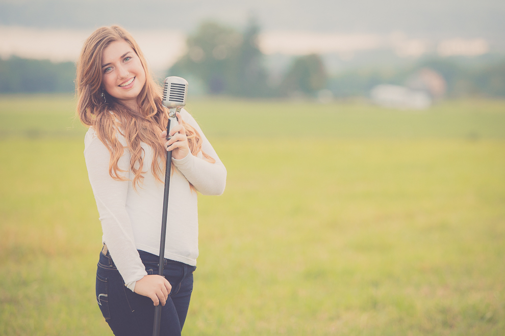 senior portrait photography of young woman posing for photographer with microphone in field in Bemus Point, NY, a town near Buffalo in WNY