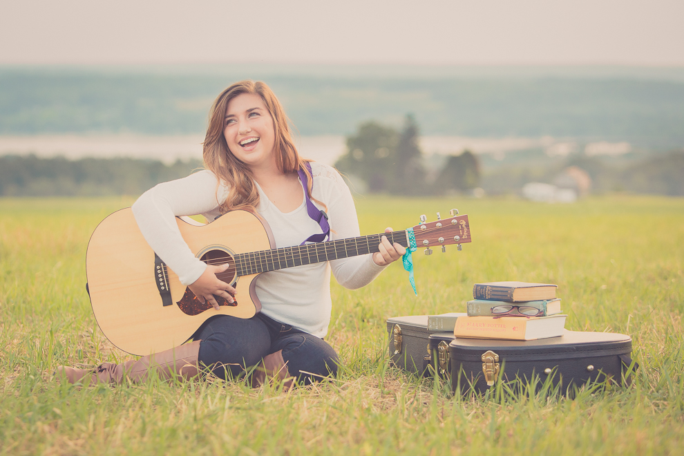 senior portrait photography of young woman laughing with guitar in field in Bemus Point, NY, a town near Buffalo in WNY