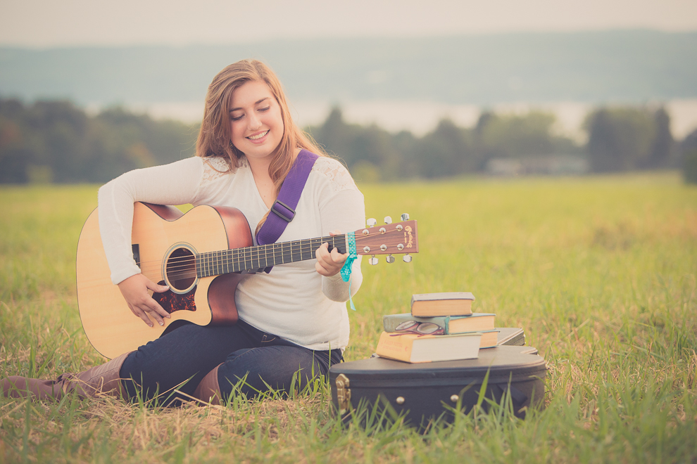 senior portrait photography of young woman playing guitar in field in Bemus Point, NY, a town near Buffalo 