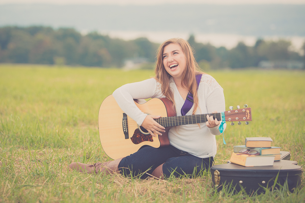 senior portrait photography of young woman laughing with guitar in field in Bemus Point, NY, a town near Buffalo 
