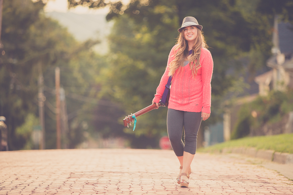 senior portrait photography of young woman walking down cobblestone street with guitar in Jamestown, NY, a city in WNY