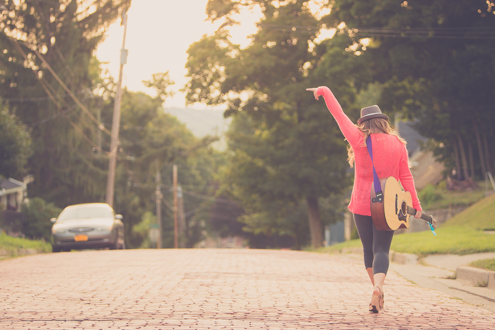 senior portrait photography of young woman walking down cobblestone street with guitar in Jamestown, NY, a city in WNY