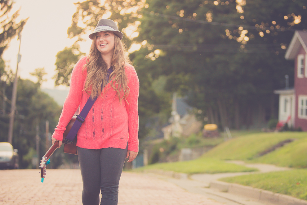 senior portrait photography of young woman walking down cobblestone street with guitar in Jamestown, NY, a city in WNY