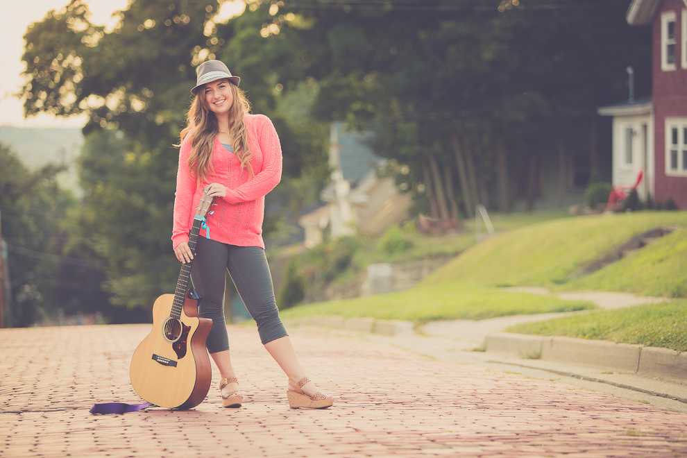 senior portrait photography of young woman posing for photographer with guitar on cobblestone street in Jamestown, NY, a city in WNY