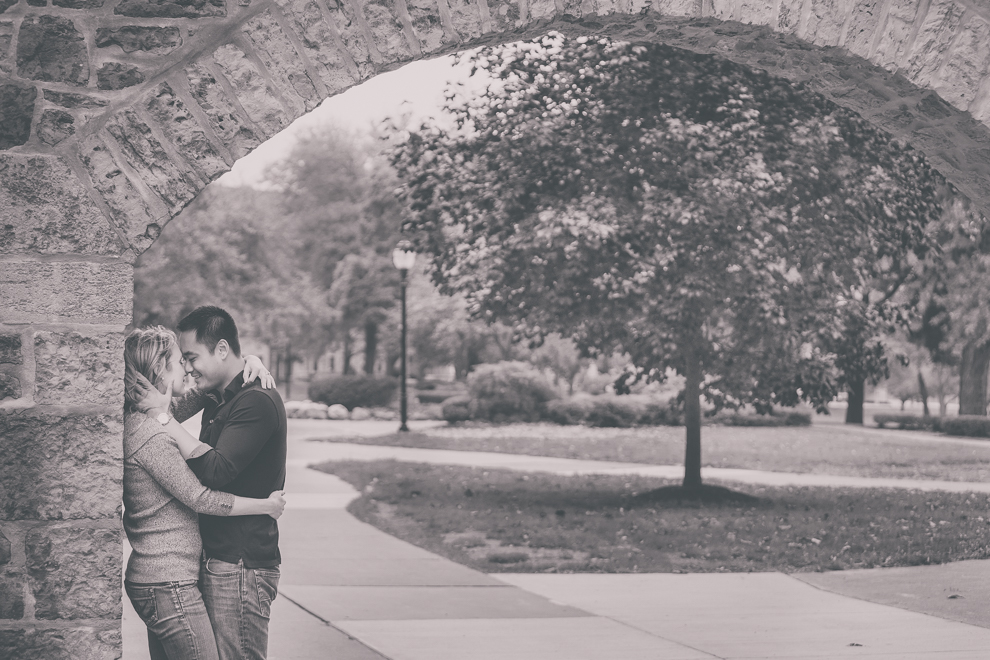 Two Niagara University Alumni snuggle under arch during their wedding engagement photography session