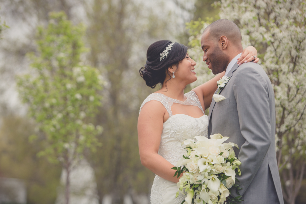 bride and groom smile at one another in garden with spring blossoms at outdoor wedding ceremony venue, the Avanti Mansion, near Buffalo, NY