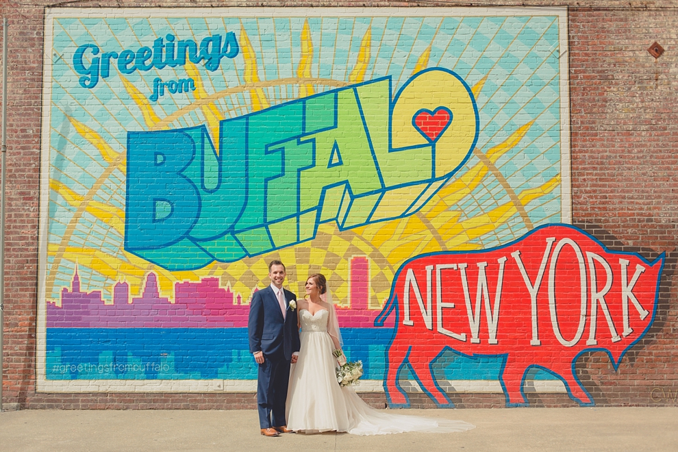 bride and groom pose for portrait near "greetings from Buffalo" mural in downtown Buffalo, NY