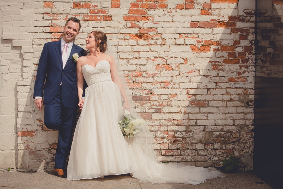 bride and groom pose for portrait near "greetings from Buffalo" mural in downtown Buffalo, NY