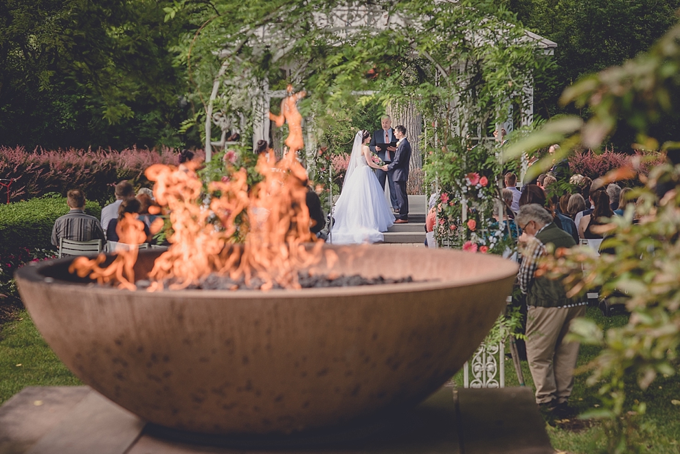 bride and groom exchange vows behind flameduring garden wedding ceremony at Samuel's Grande Manor near Buffalo, NY