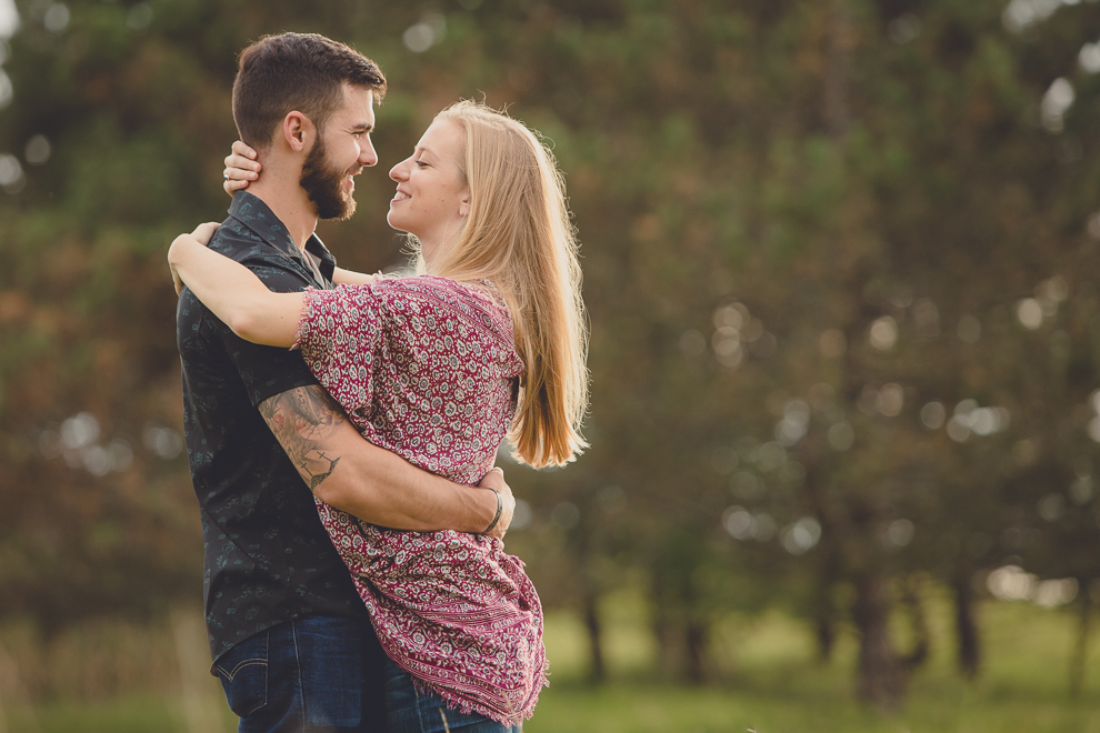 engagement photos of couple embracing and laughing in front of pine trees in field at Tifft Nature Preserve in Buffalo, NY