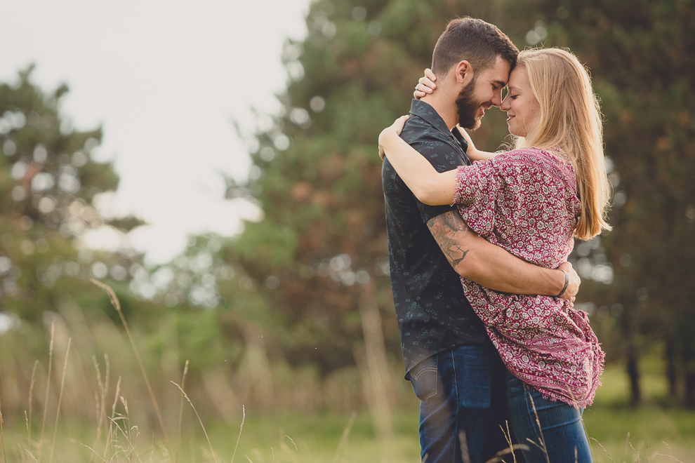engagement photos of couple embracing and touching foreheads in front of pine trees in field at Tifft Nature Preserve in Buffalo, NY