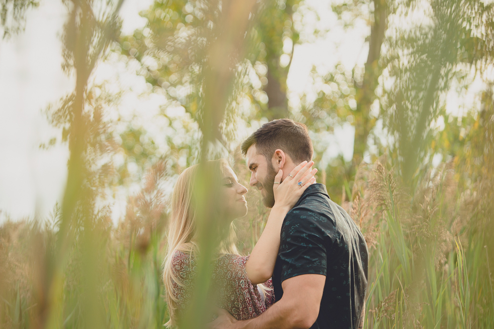 bride and groom smile at each other while standing among cat tails in Tifft Nature Preserve in Buffalo, NY during their engagement photography session