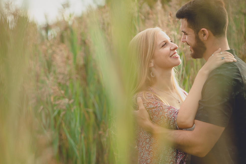 bride and groom smile at each other while standing among cat tails in Tifft Nature Preserve in Buffalo, NY during their engagement photography session