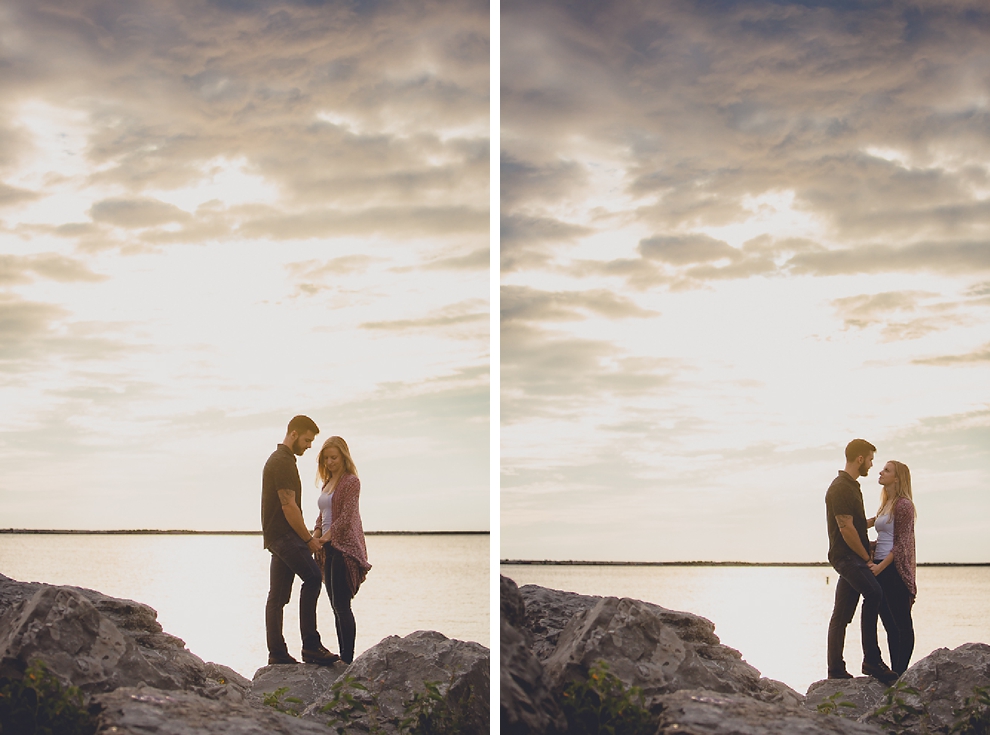 bride and groom stand on rocks as the sunsets behind them during wedding engagement photography session on Gallagher Beach at Buffalo Harbor