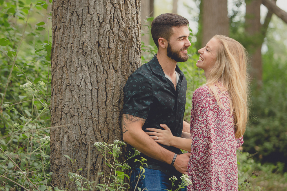 engagement photography of couple leaning on tree in woods at Tifft Nature Preserve in Buffalo, NY