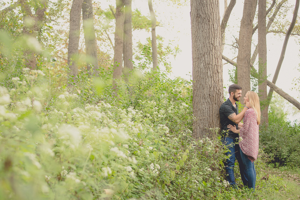 engagement photography of couple leaning on tree in woods at Tifft Nature Preserve in Buffalo, NY