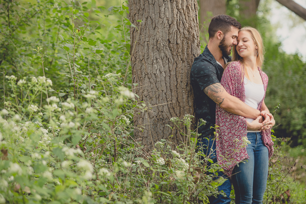 engagement photography of couple leaning on tree in woods at Tifft Nature Preserve in Buffalo, NY