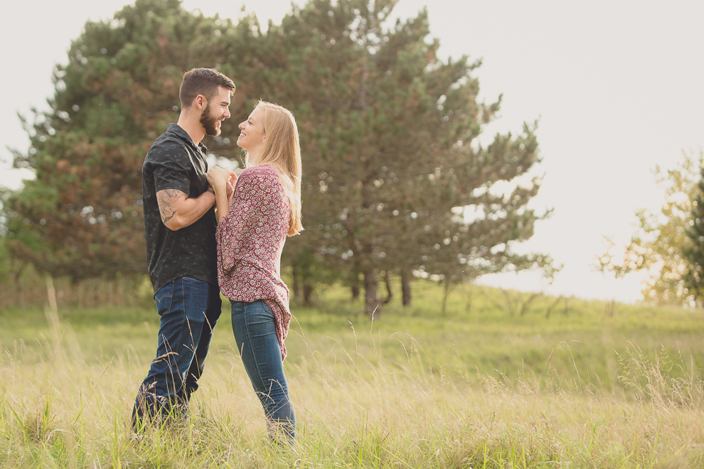 engagement photos of couple holding hands and looking at each other in front of pine trees in field at Tifft Nature Preserve in Buffalo, NY