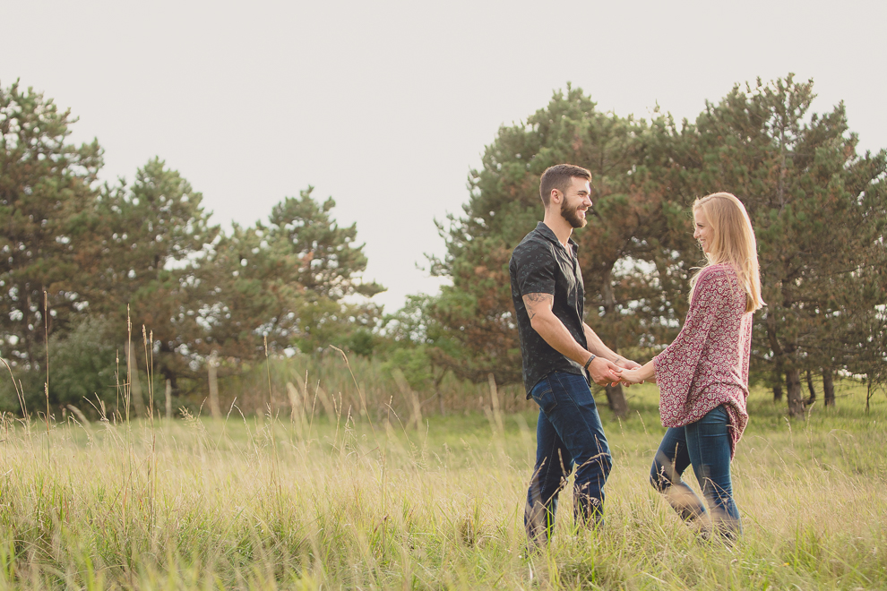 engagement photos of couple holding hands and looking at each other in front of pine trees in field at Tifft Nature Preserve in Buffalo, NY