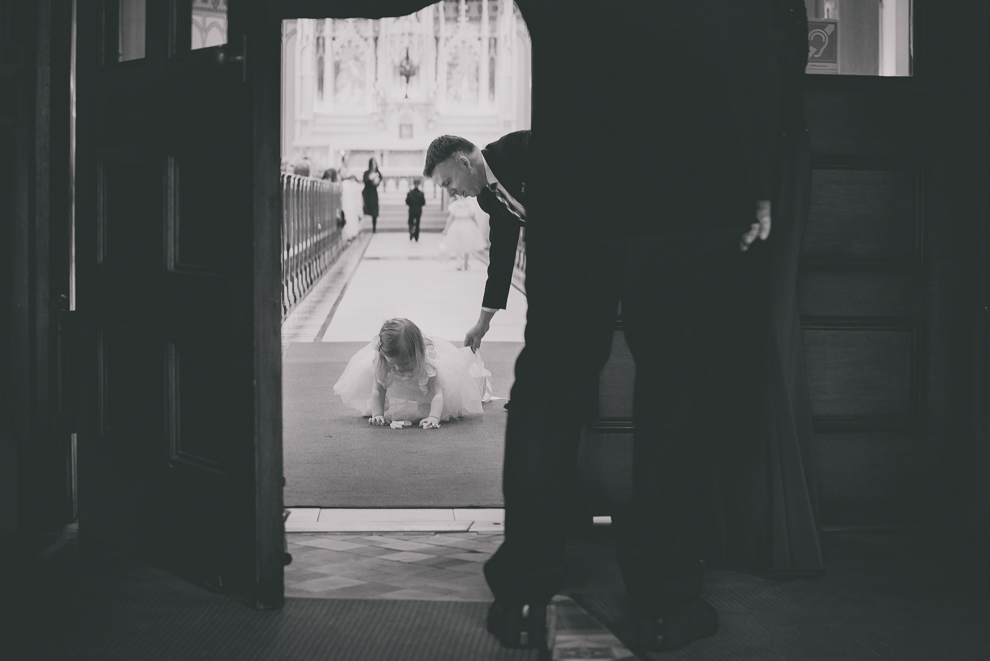 flower girl picks up flowers during wedding ceremony at St. Louis Church in Buffalo, NY