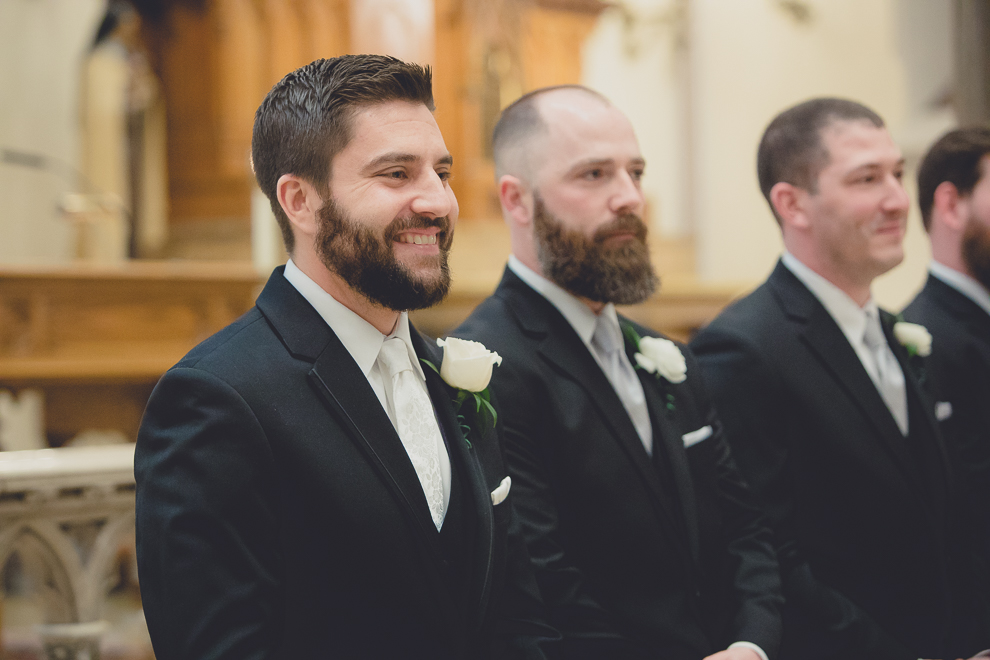 groom smiles at bride as she walks down aisle during wedding ceremony at St. Louis Church in Buffalo, NY