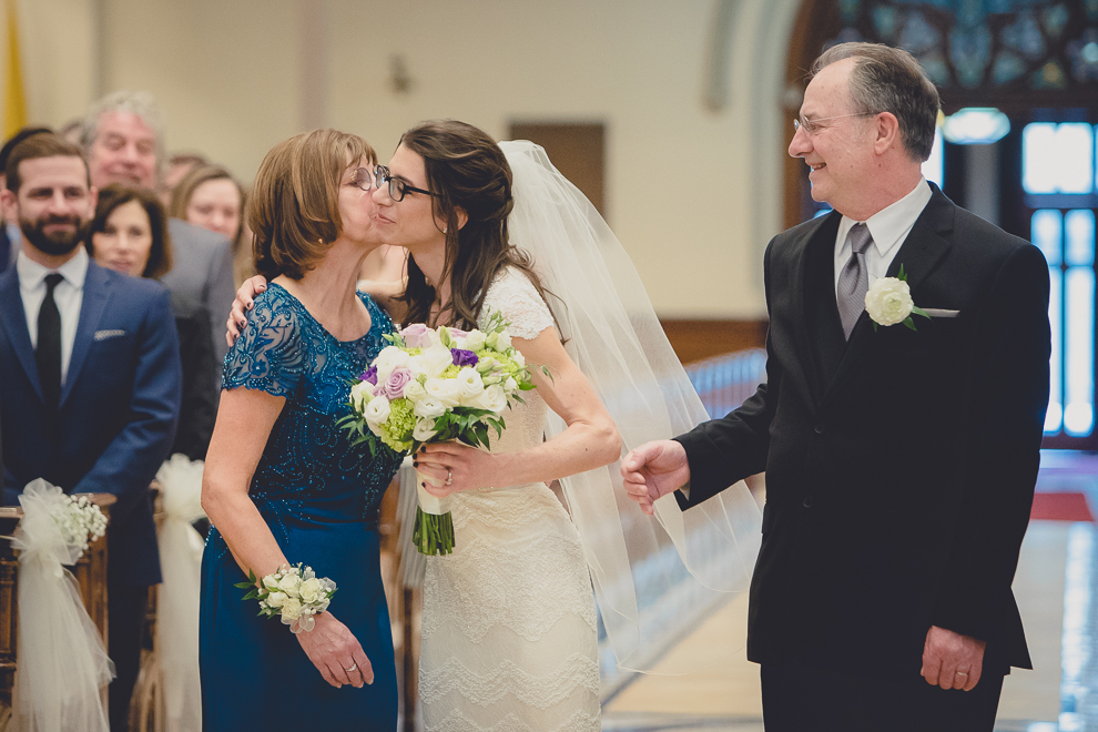 bride kisses mother and father after walking down the aisle during wedding ceremony at St. Louis Church in Buffalo, NY