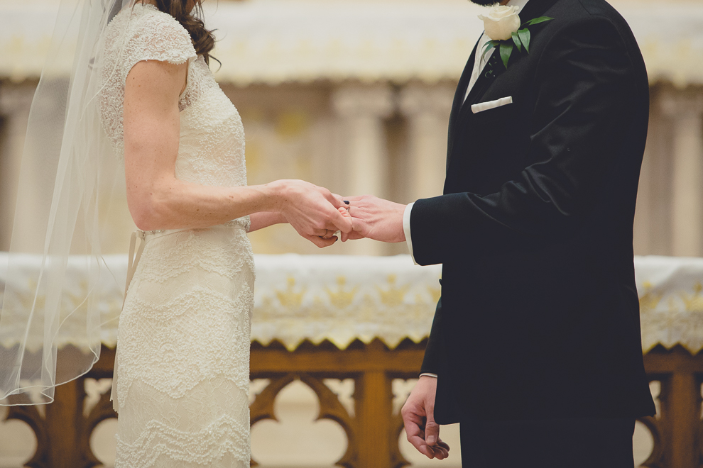 bride places ring on grooms finger during wedding ceremony at St. Louis Church in Buffalo, NY