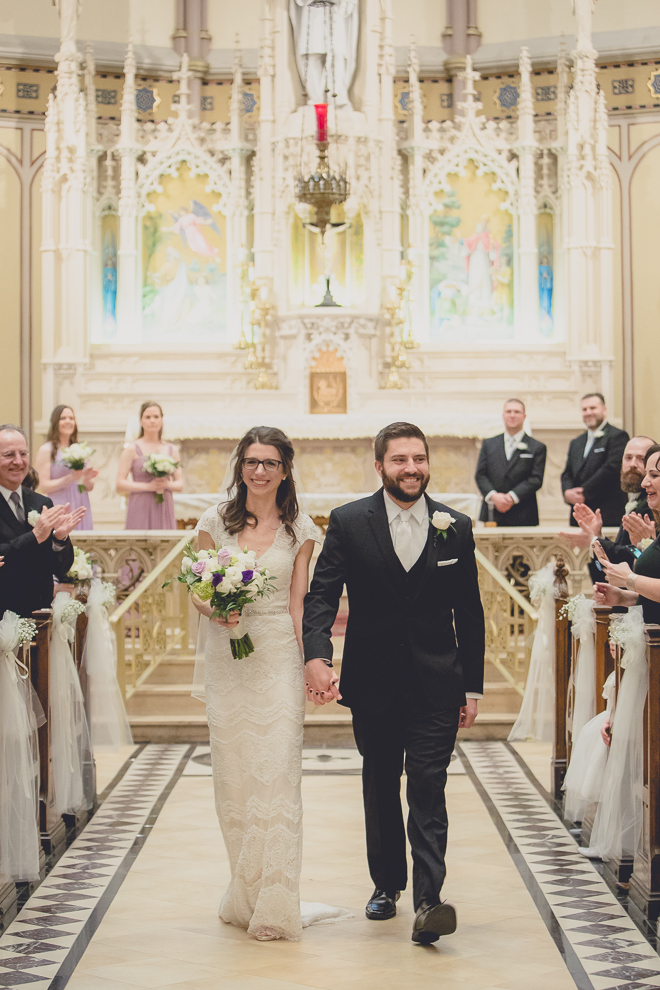 bride and groom smile as they walk down aisle during wedding ceremony at St. Louis Church in Buffalo, NY