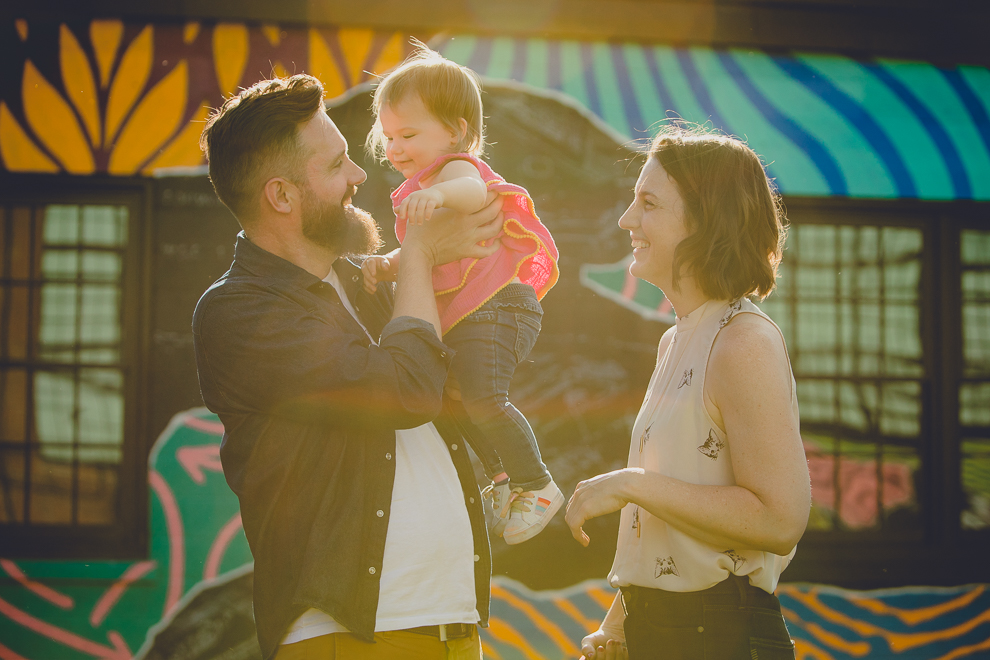 father lifts daughter during family portrait photography session in front of murals on Chandler St. in Buffalo, NY