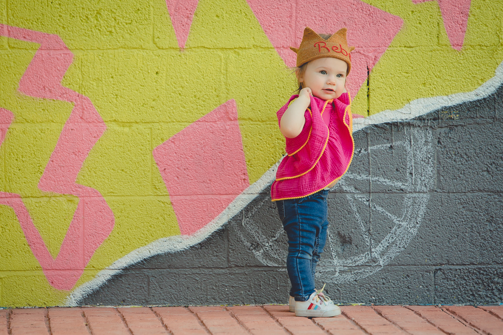 small child shows belly while wearing rebel hat during photography session in front of murals on Chandler St. in Buffalo, NY