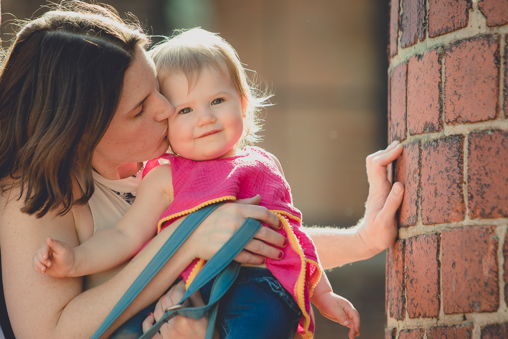 mother kisses daughter during family portrait photography session in front of murals on Chandler St. in Buffalo, NY