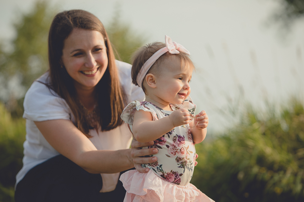 mom holds up baby as she attempts first steps during family portrait photography session in at Tifft Nature Preserve in Buffalo, NY