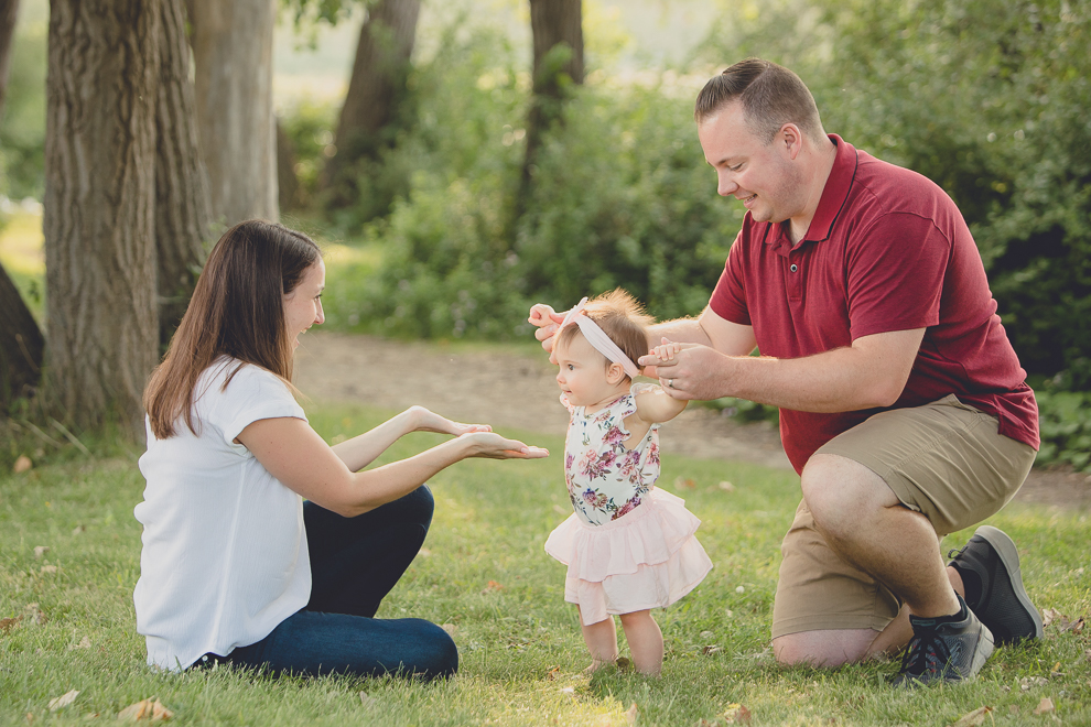father holds up baby as she tries to take first steps during family portrait photography session in at Tifft Nature Preserve in Buffalo, NY