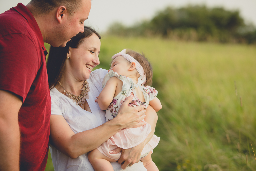 mom and dad smile at baby during family portrait photography session in at Tifft Nature Preserve in Buffalo, NY