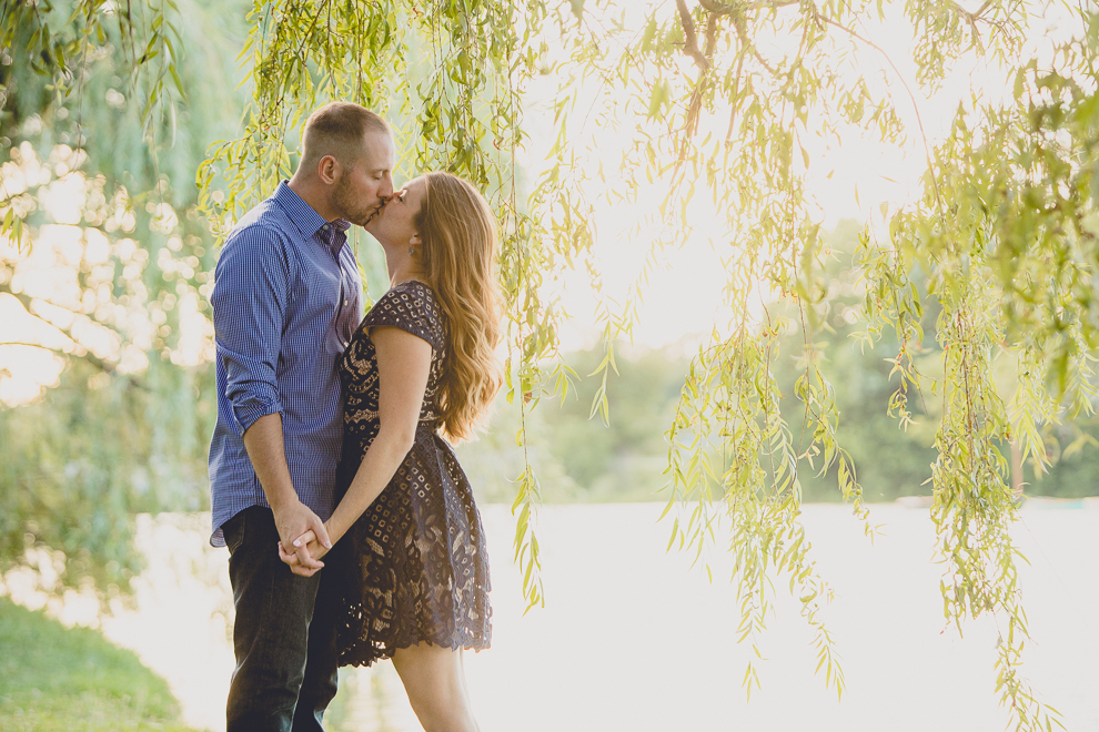 engaged couple kisses beneath willow tree by Hoyt Lake for engagement photography at hotel henry & delaware park in Buffalo, NY