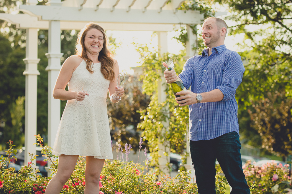 engaged couple pops champagne in rose garden for wedding engagement photography at hotel henry & delaware park in Buffalo, NY