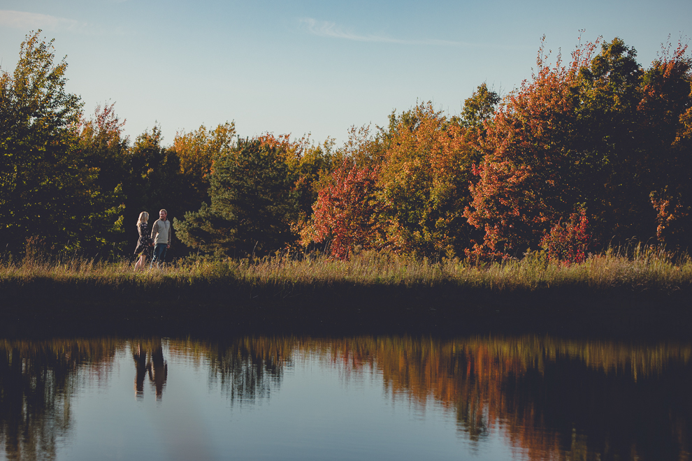 bride and groom walk past reflective pond during wedding engagement photos among fall foliage at their property in Ellicottville, NY