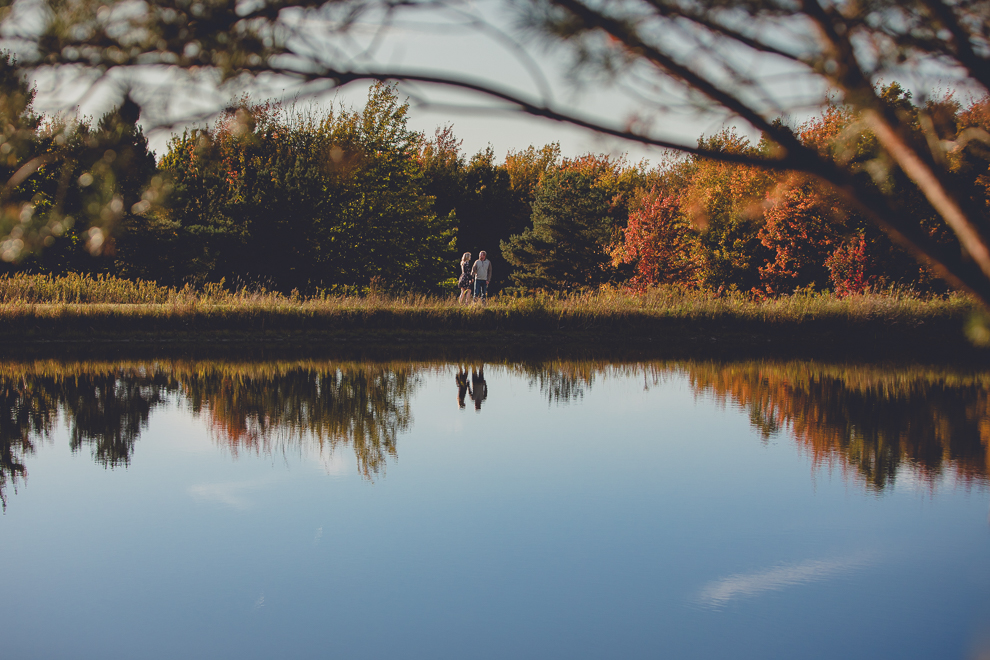 bride and groom walk past reflective pond during wedding engagement photos among fall foliage at their property in Ellicottville, NY