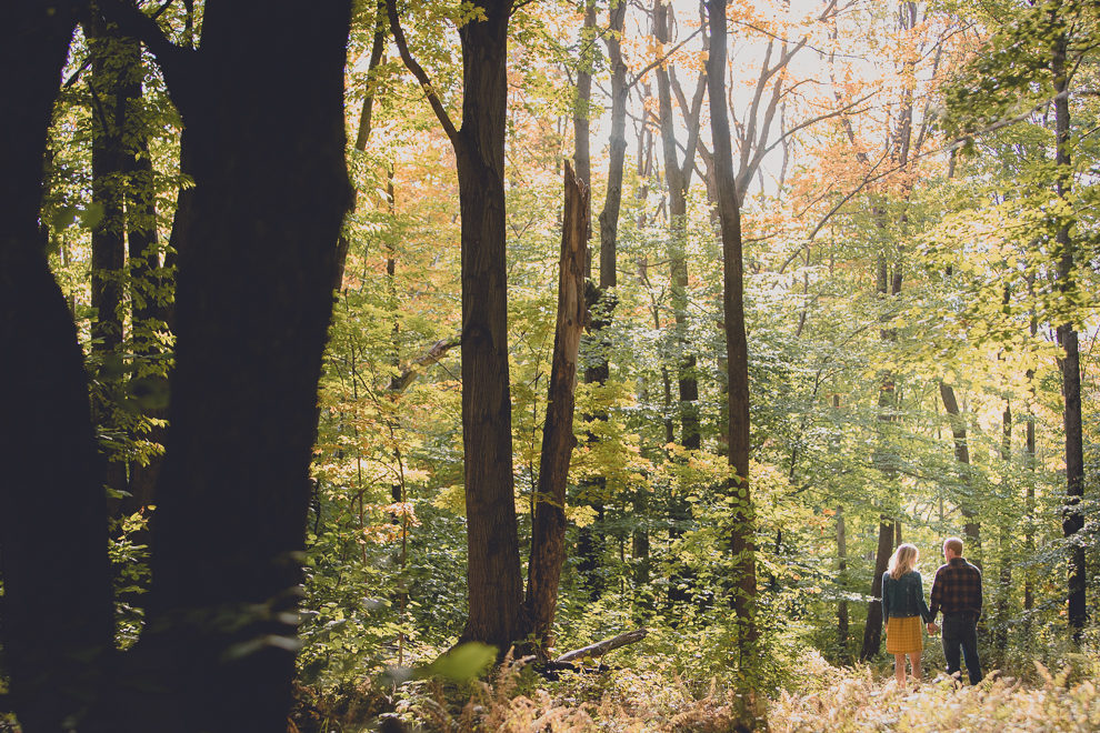 bride and groom walk while holding hands during wedding engagement photos among fall foliage at their property in Ellicottville, NY