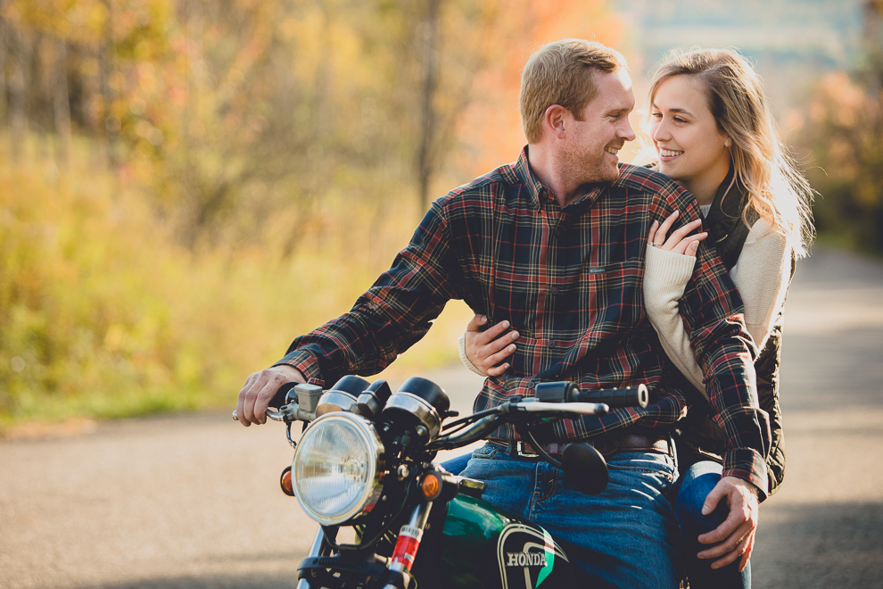 bride and groom sit on motorcycle during wedding engagement photos among fall foliage at their property in Ellicottville, NY