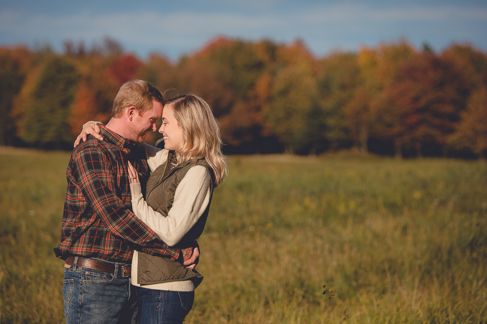bride and groom hug in field during wedding engagement photos among fall foliage at their property in Ellicottville, NY