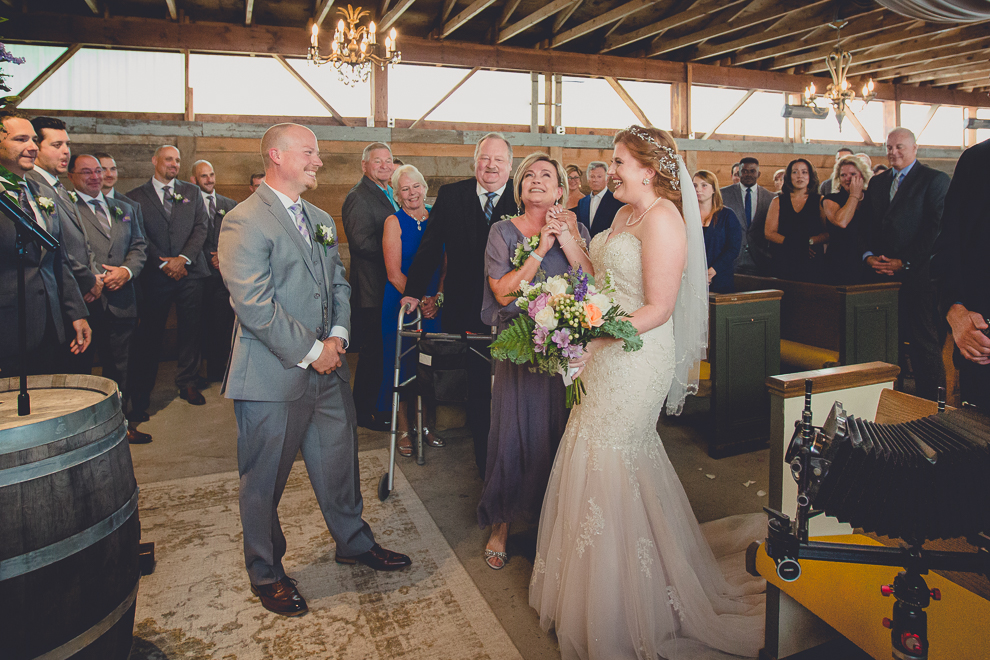 mom clenches brides hand at end of aisle before "giving her away" at wedding ceremony in converted stables at a Hayloft in the Grove wedding in East Aurora, near Buffalo, NY
