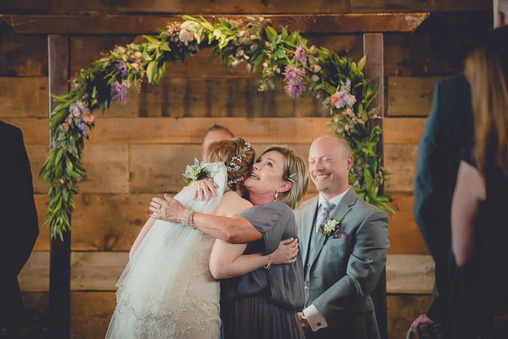 bride and mom hug at wedding ceremony in converted stables at a Hayloft in the Grove wedding in East Aurora, near Buffalo, NY