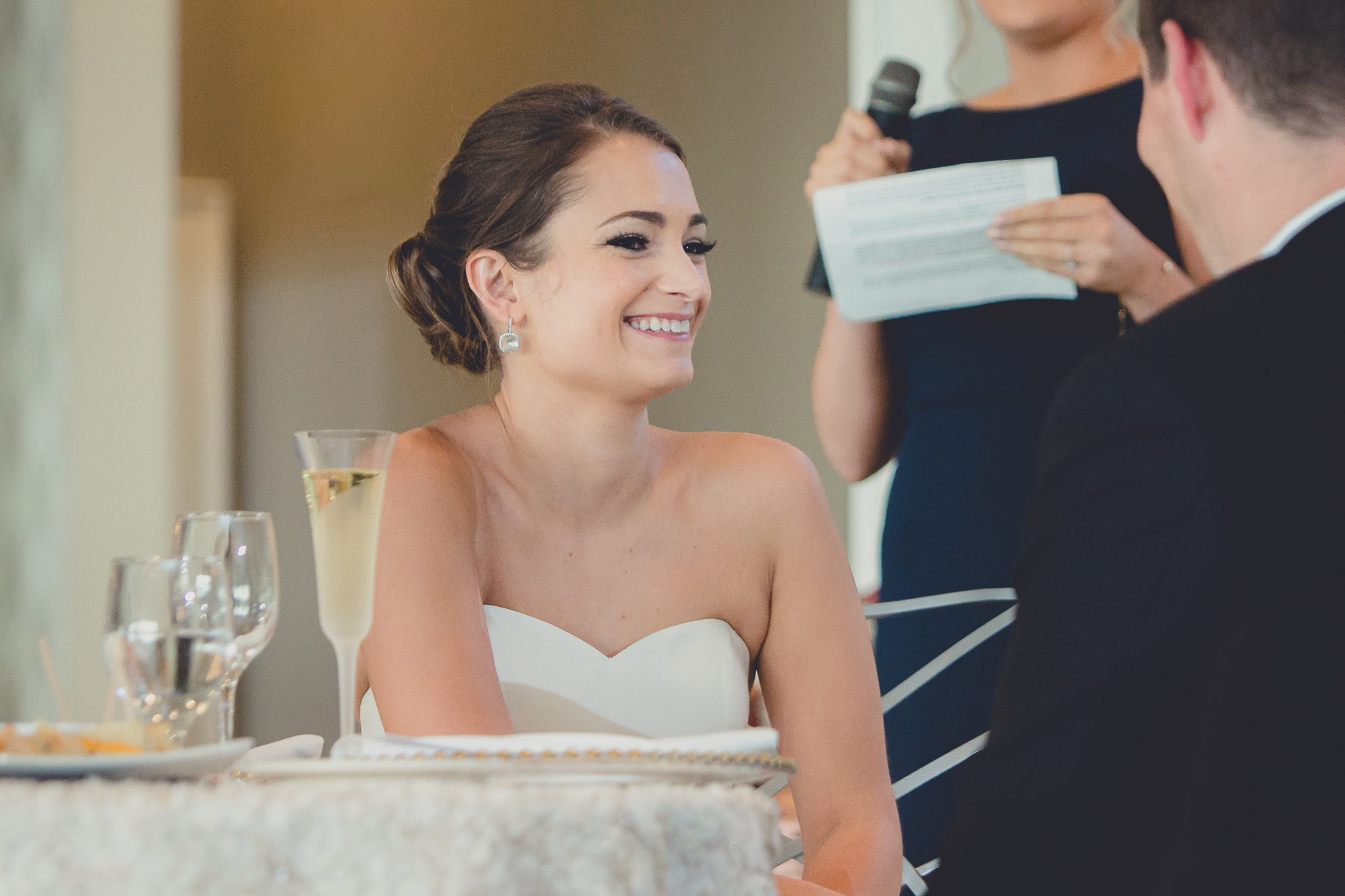 bride smiles at groom during speech at wedding reception at Niagara Falls Country Club in Lewiston, NY