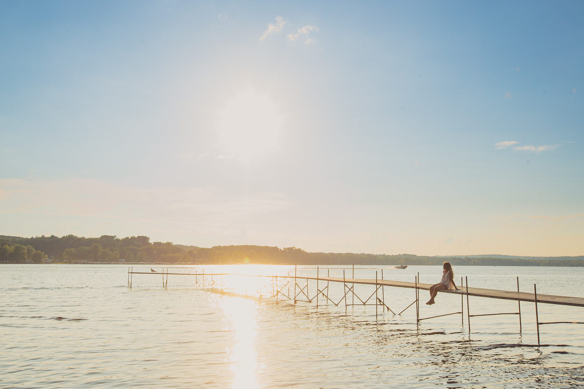 Dana sits on dock at sunset during her senior session in Long Point State Park near Buffalo, NY