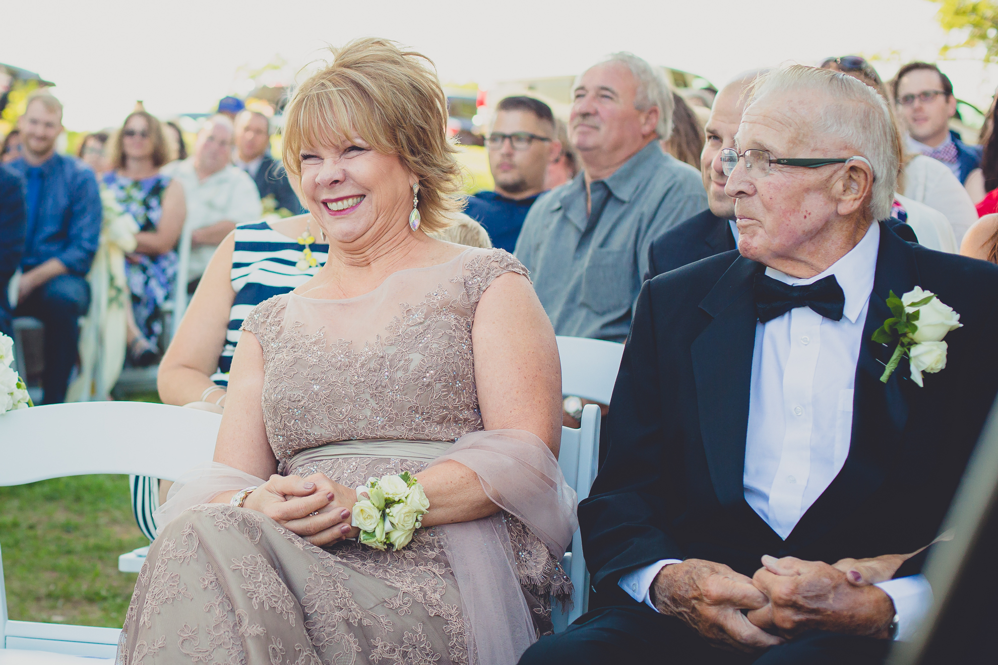 mother and grandfather smile at bride and father as they walk down aisle at Spring Lake Winery in Niagara County before wedding near Buffalo, NY