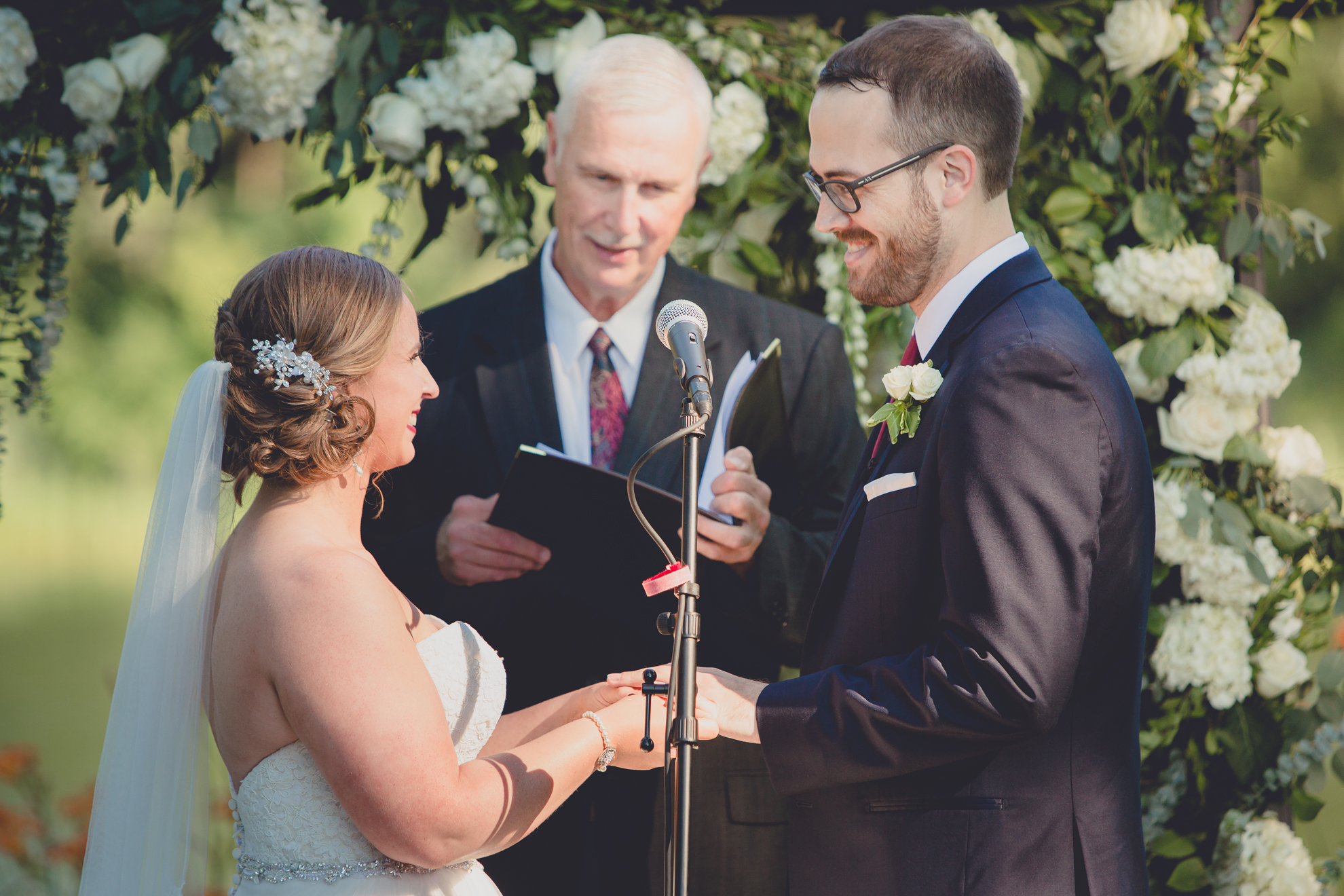 bride and groom smile at each other while exchanging vows during wedding outdoor wedding ceremony at Spring Lake Winery in Lockport, NY