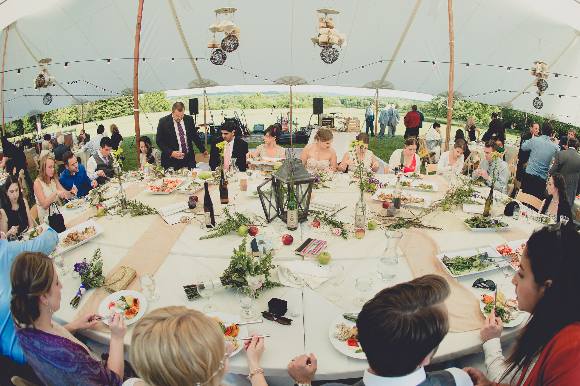 wedding guests sit for dinner around giant table during tented reception at small wedding at Knox Farm near Buffalo, NY
