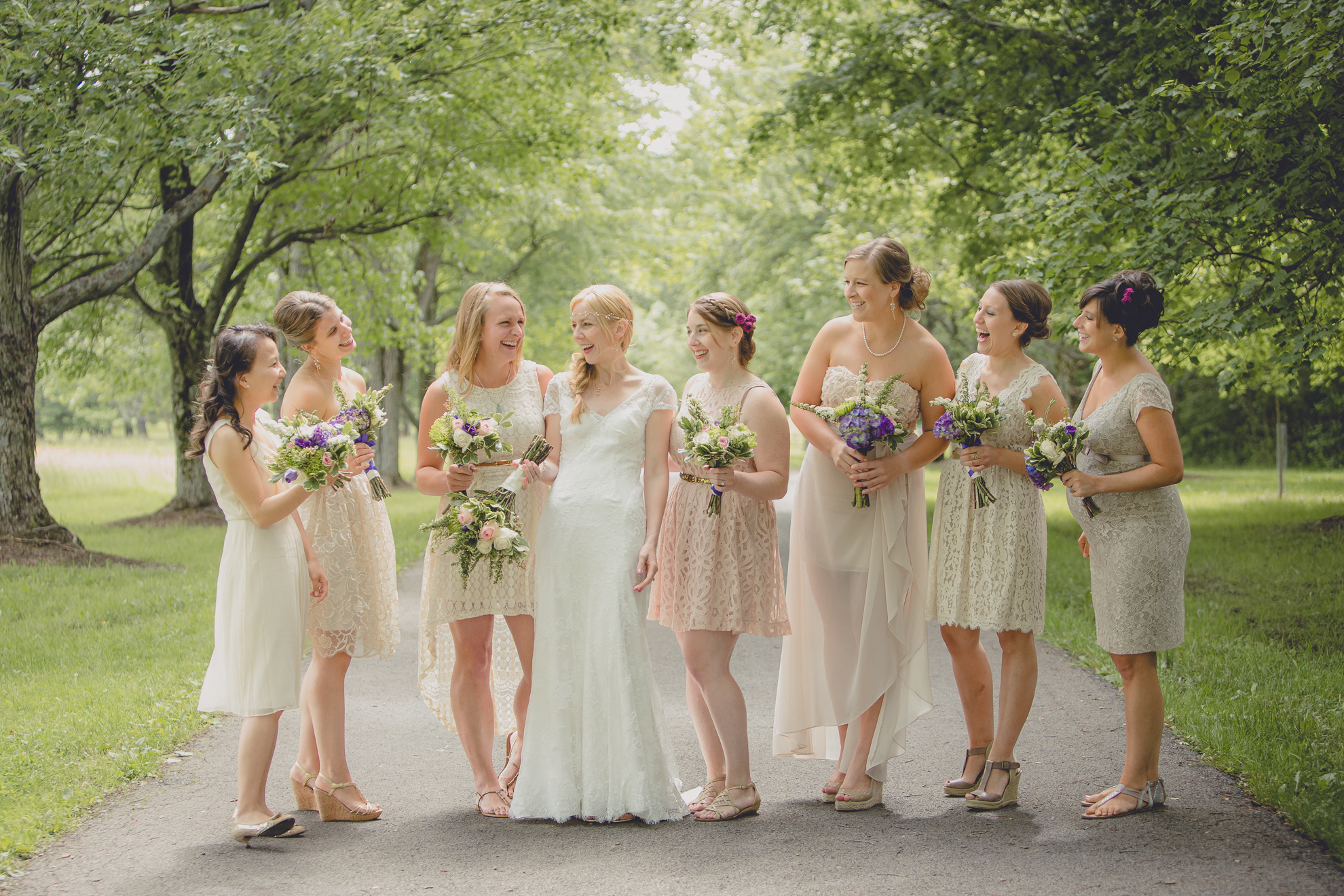 bridesmaids laugh as they stand for portraits on tree lined road at small wedding at Knox Farm near Buffalo, NY